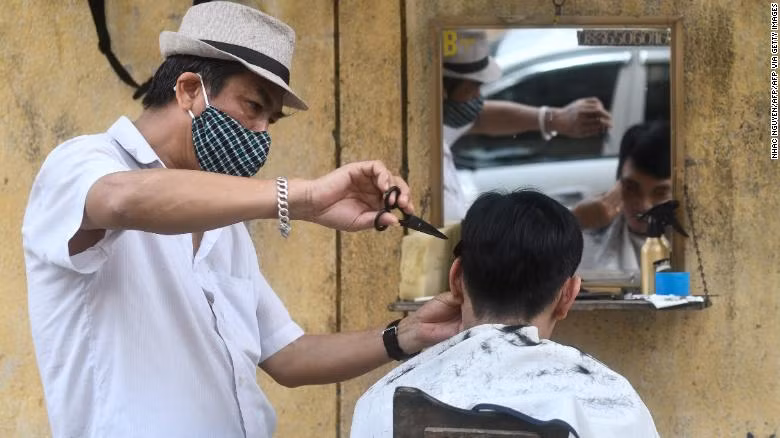 How Vietnam managed to keep its coronavirus death toll at zero? ảnh 5 A roadside barber donning a face mask gives a haircut to a customer in Hanoi.