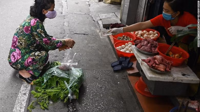 How Vietnam managed to keep its coronavirus death toll at zero? ảnh 2 A woman practises social distancing while shopping for groceries from behind a line at a wet market in Hanoi.