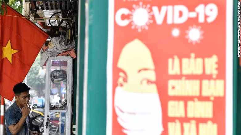 A propaganda poster on preventing the spread of the coronavirus is seen on a wall as a man smokes a cigarette along a street in Hanoi.