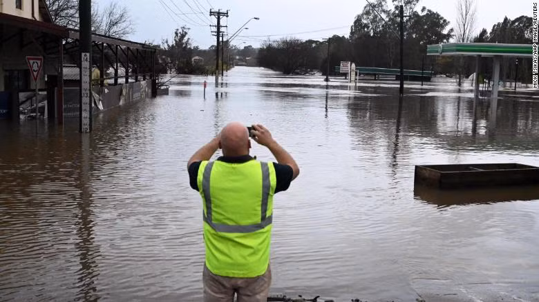 A local takes a photo of a road inundated by floodwaters in Camden in South Western Sydney, Sunday, July 3, 2022.
