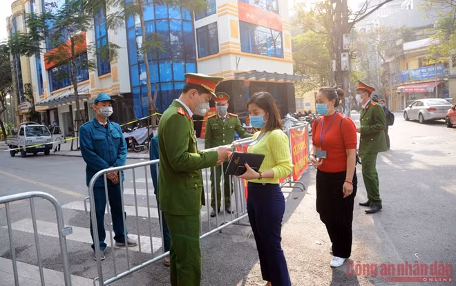 A police officer is checking access cards of on-duty people at the entrance gate of the quarantine zone.