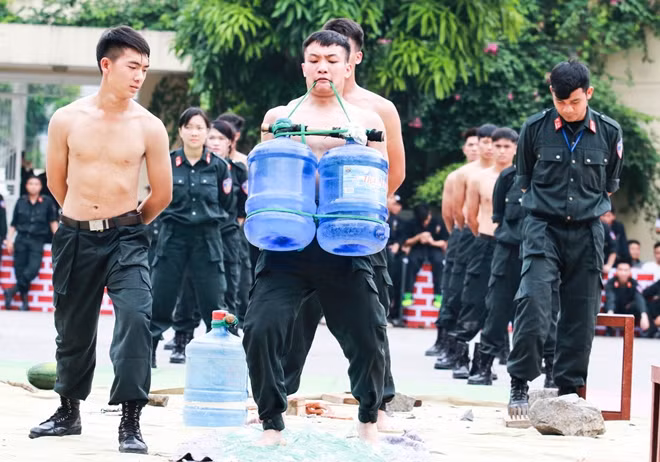 Police officer lifting a heavy object off the ground with teeth while walking on a pile of broken glass.