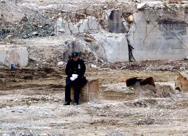 A lone police officer sits away from where family members of the victims of the September 11 attacks on the World Trade Center were gathering at the base of the "Ground Zero," September 11, 2002. REUTERS/Mike Segar