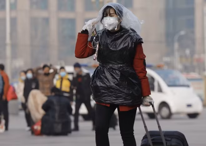 A passenger at a Beijing railway station covers her head and body with plastic bags for added protection against the coronavirus. Photo: EPA-EFE