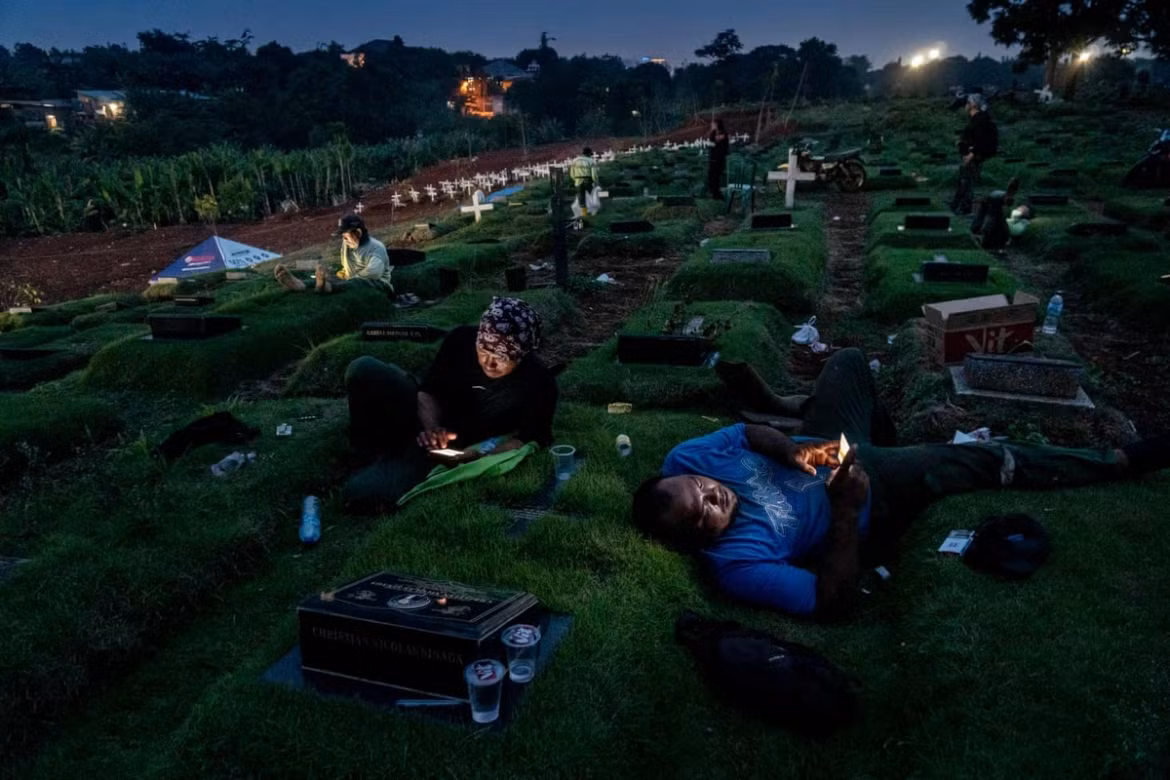 A photo by Ares Jonekson Saragi makes the shortlist in the street photography category. The theme is “Night in Pandemic Time” and taken at the Pondok Ranggon Cemetery in Jakarta during the afternoon. Viewers can see the funeral officers having a break, watching videos on their smartphones, and chatting with their families.