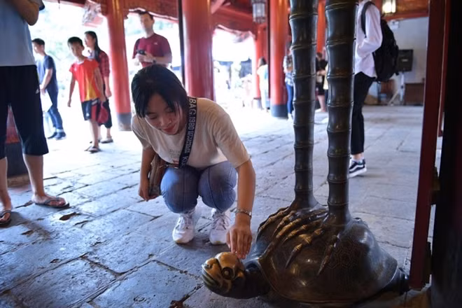 Some students rubs stone turtles' heads. These turtle statues carry the names of doctorate students from 1442 to 1779 on them, and many believe this practice brings them good luck.