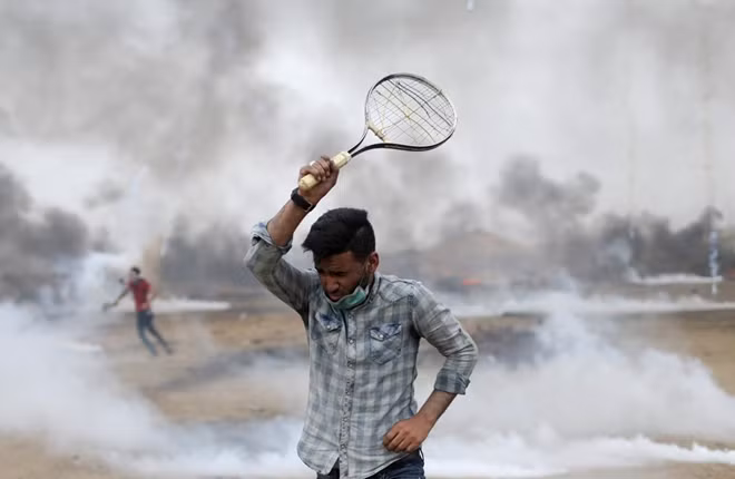 A demonstrator uses a racket to return tear gas canisters fired by Israeli troops during a protest where Palestinians demand the right to return to their homeland, at the Israel-Gaza border in the southern Gaza Strip, May 4, 2018. REUTERS/Ibraheem Abu Mustafa.