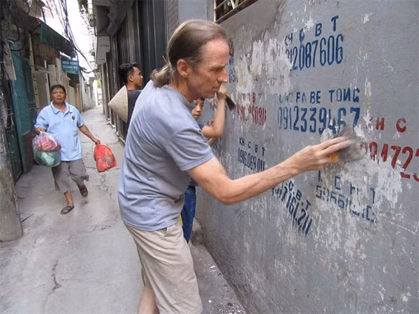 Elbow grease: Paul George Harding and local children scrap dirty advertisements pasted on walls along Nguyen Ngoc Vu Street.— Photo: Bach Lien/VNS