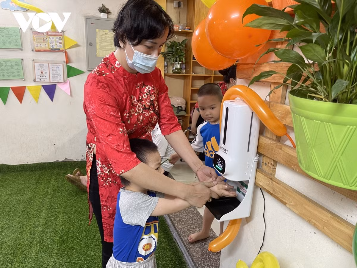A teacher guides children to sanitize their hands before entering class.