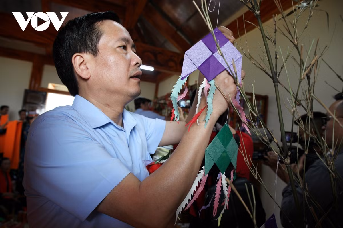 A participant hangs a small paper kite on a branch as they pray for good luck during the new harvest.