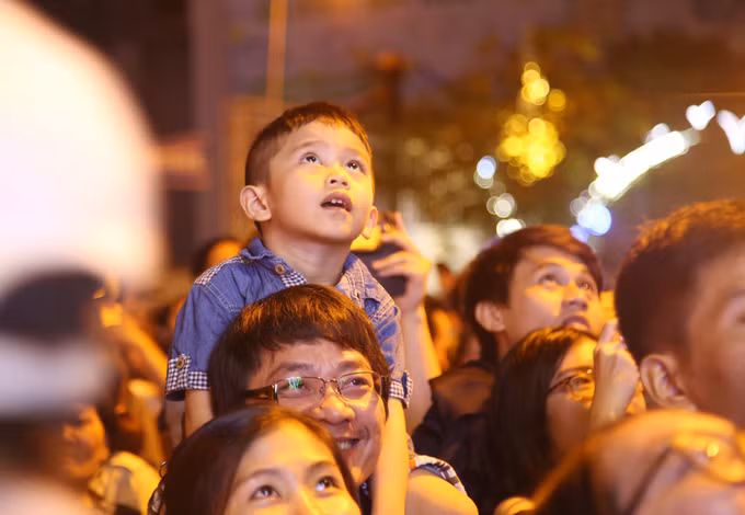 A boy sits on his fathers shoulders as the family watches the fireworks show.